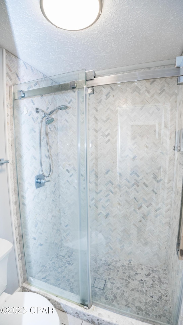 full bathroom featuring a textured ceiling, a shower stall, and toilet