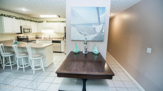 kitchen with appliances with stainless steel finishes, a textured ceiling, light tile patterned flooring, and a sink