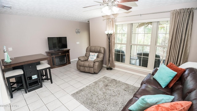 living area featuring visible vents, light tile patterned flooring, baseboards, a textured ceiling, and ceiling fan
