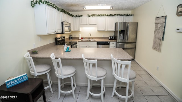 kitchen featuring a peninsula, a sink, visible vents, white cabinetry, and appliances with stainless steel finishes