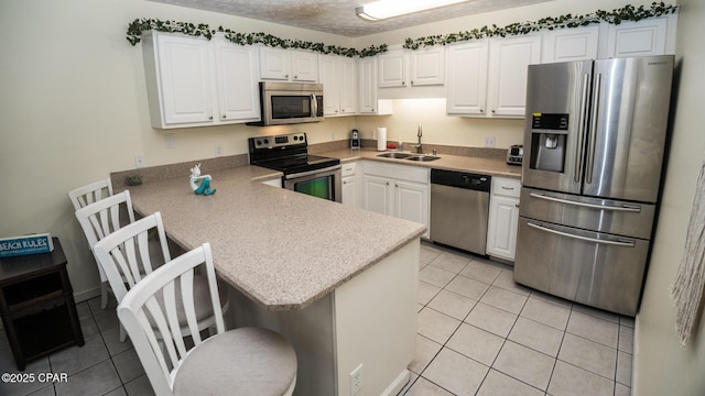kitchen featuring a sink, light tile patterned floors, white cabinetry, a peninsula, and appliances with stainless steel finishes