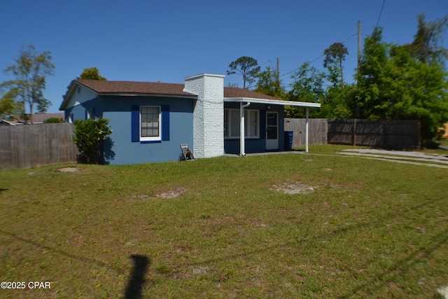 rear view of house featuring stucco siding, a lawn, a chimney, and fence