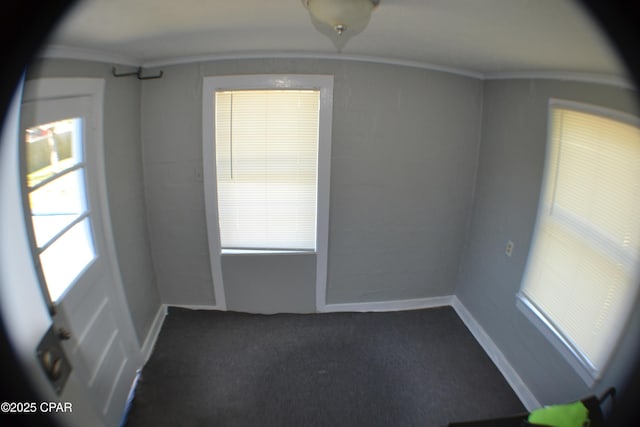 empty room featuring dark colored carpet, a healthy amount of sunlight, and ornamental molding