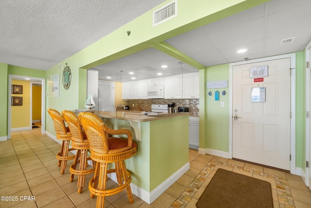 10509 Front Beach Rd Unit 300, Panama City Beach, FL 32407 - kitchen with white appliances, a breakfast bar, white cabinetry, visible vents, and light tile patterned flooring