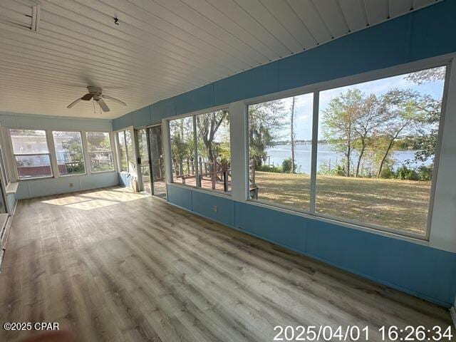 unfurnished sunroom featuring wood finished floors, a water view, and a ceiling fan