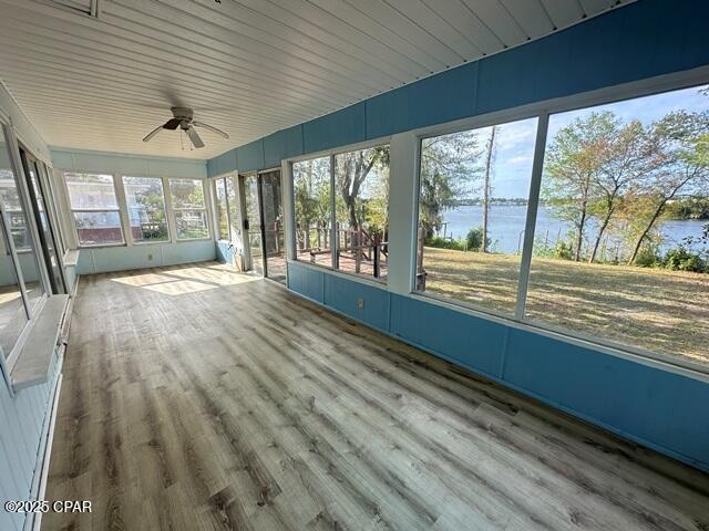 unfurnished sunroom with a ceiling fan and a water view