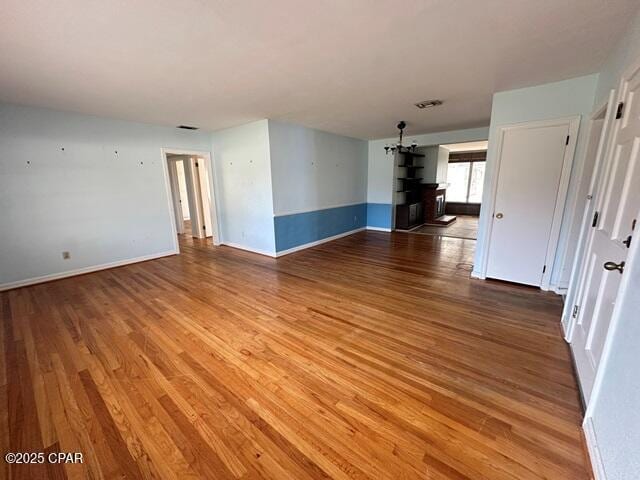 unfurnished room with light wood-type flooring, baseboards, visible vents, and a notable chandelier
