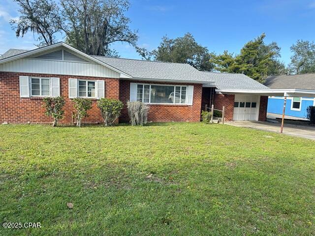 ranch-style house featuring brick siding, an attached garage, a front yard, and driveway