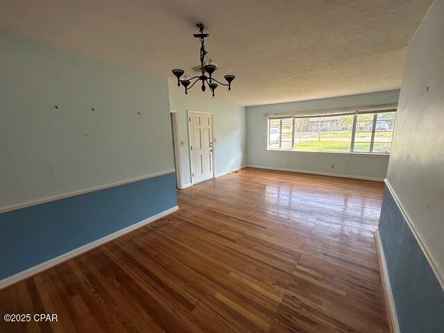 unfurnished room featuring baseboards, wood finished floors, and a chandelier