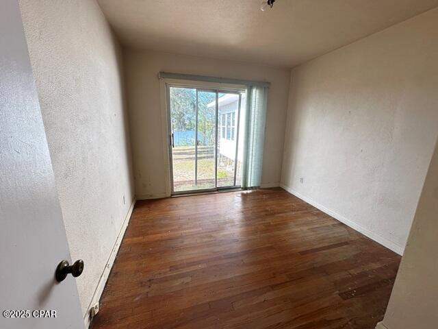 unfurnished room featuring a textured wall, baseboards, and wood finished floors