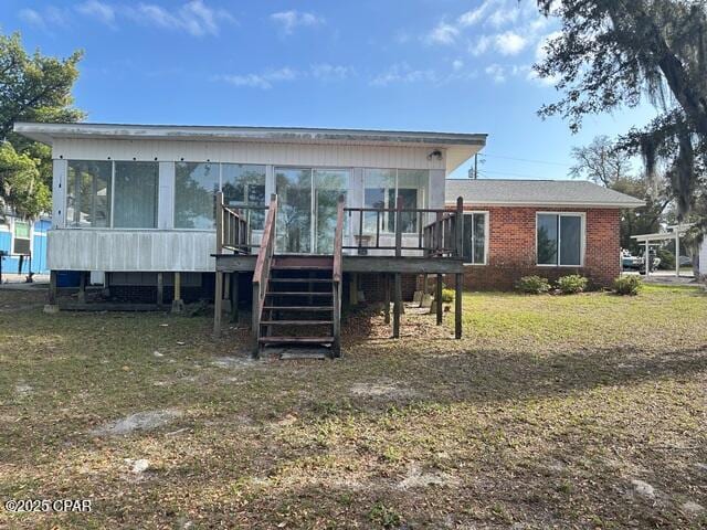 rear view of property with stairway, a yard, brick siding, a sunroom, and a deck