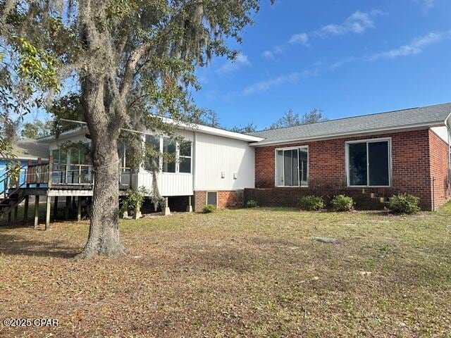 view of front of property with brick siding, a sunroom, a front lawn, and a deck