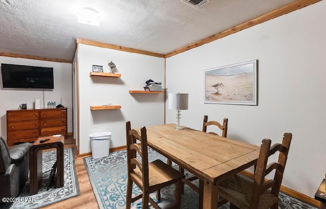dining area featuring baseboards, a textured ceiling, visible vents, and light wood-style floors