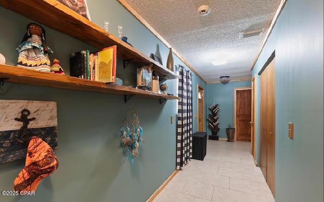 hallway with a textured ceiling, baseboards, visible vents, ornamental molding, and light tile patterned floors