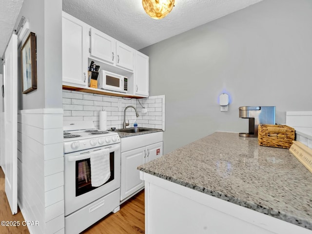 kitchen with white cabinets, white appliances, a sink, and light wood-style floors