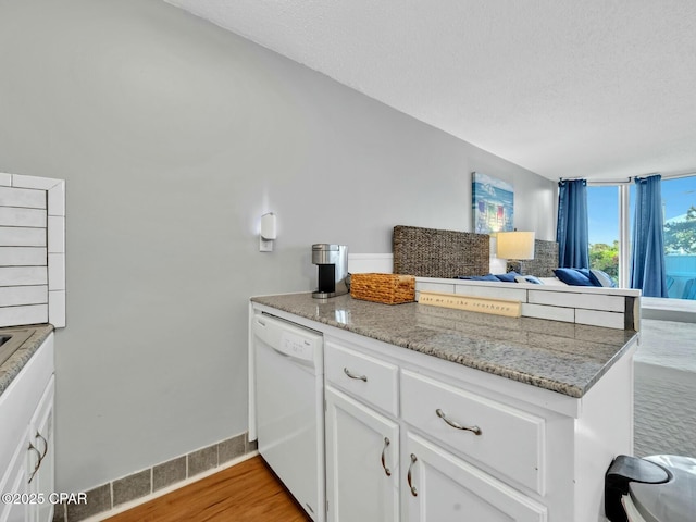kitchen with white cabinets, a peninsula, light wood finished floors, white dishwasher, and light stone counters