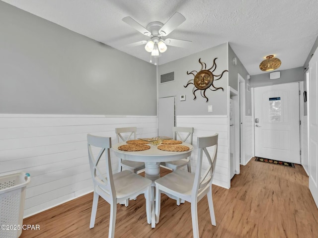 dining space featuring a textured ceiling, wainscoting, visible vents, light wood-style floors, and ceiling fan