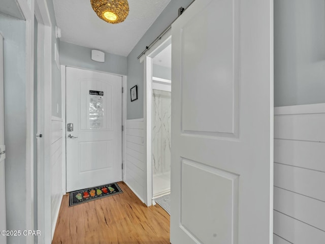 interior space with a barn door, light wood-type flooring, and a wainscoted wall