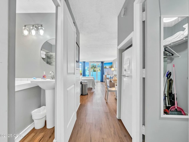 hall featuring wood finished floors, a textured ceiling, baseboards, and a sink
