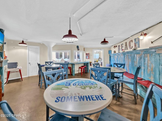 dining space with decorative columns, finished concrete floors, and a textured ceiling