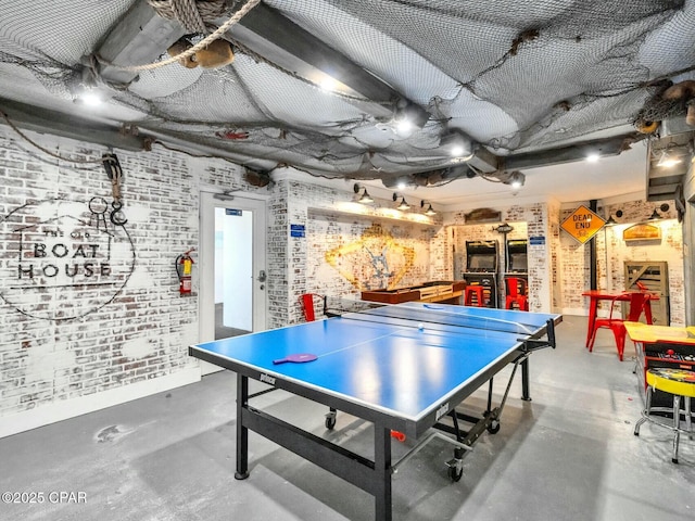 game room with brick wall, baseboards, and concrete flooring
