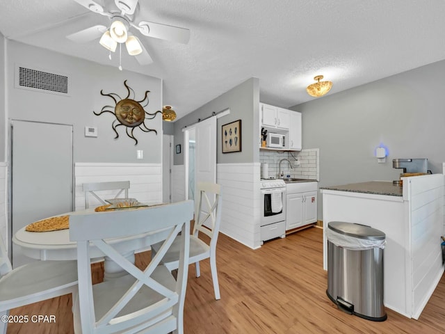 dining room featuring light wood finished floors, visible vents, ceiling fan, and a barn door
