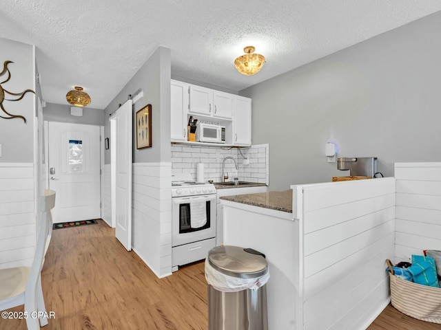 kitchen with a textured ceiling, a sink, white appliances, light wood-style flooring, and white cabinets