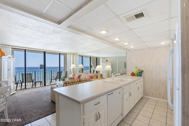 kitchen with white dishwasher, a sink, light tile patterned flooring, a peninsula, and a water view