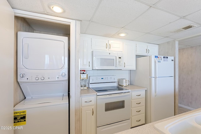 kitchen featuring white appliances, estacked washer and dryer, a drop ceiling, light countertops, and white cabinetry