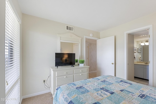 bedroom with baseboards, light carpet, and ensuite bath