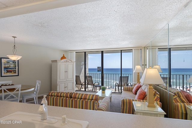 living area featuring expansive windows, a textured ceiling, a water view, healthy amount of natural light, and baseboards