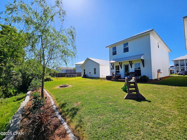 rear view of house featuring a fire pit, fence, and a lawn