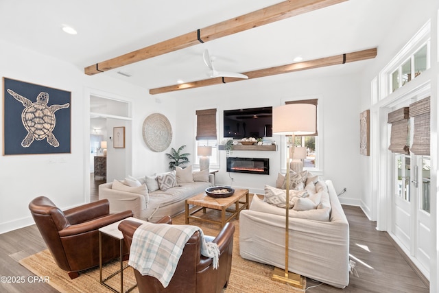 living area with a ceiling fan, beam ceiling, wood finished floors, a glass covered fireplace, and recessed lighting