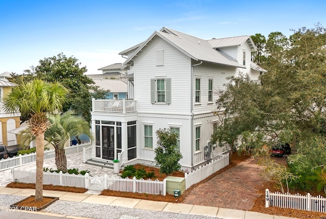 exterior space with a fenced front yard, a sunroom, metal roof, and a balcony