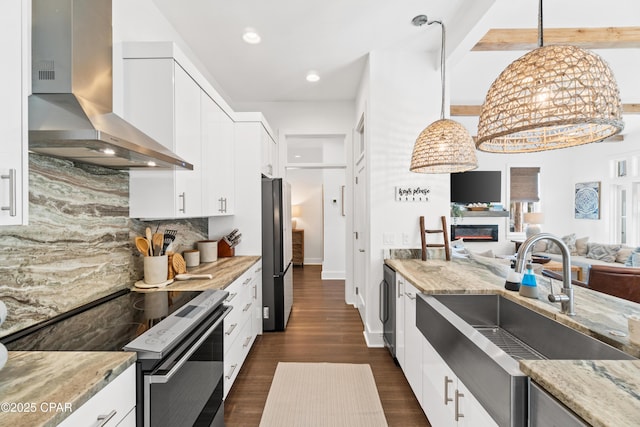 kitchen with freestanding refrigerator, light stone countertops, wall chimney range hood, electric range oven, and a sink
