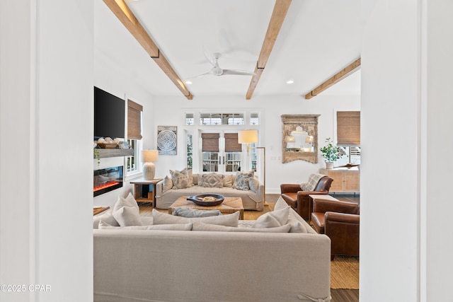 living room with a glass covered fireplace, wood finished floors, beam ceiling, baseboards, and a ceiling fan
