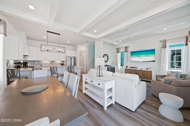 living area featuring ceiling fan with notable chandelier, beam ceiling, wood finished floors, and recessed lighting