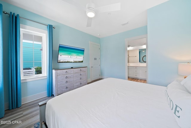 bedroom featuring baseboards, ensuite bath, wood finished floors, and ceiling fan
