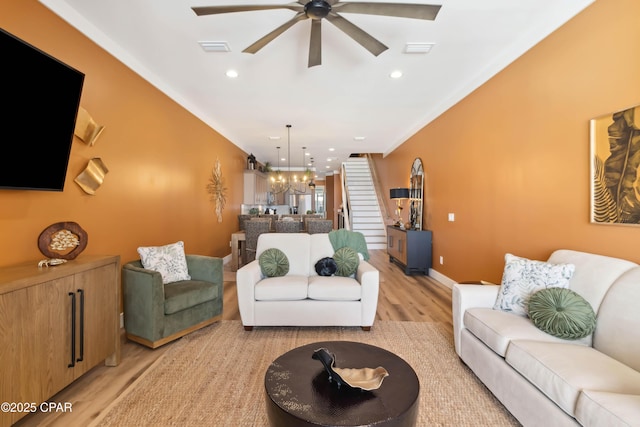 living room featuring stairs, light wood-style floors, visible vents, and ceiling fan with notable chandelier