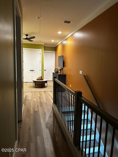 corridor featuring an upstairs landing, wood finished floors, visible vents, and recessed lighting