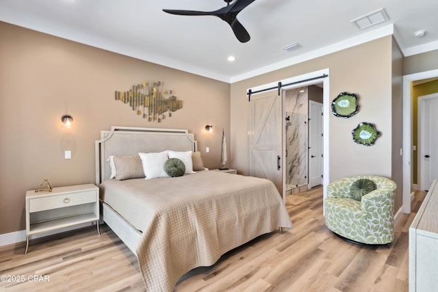 bedroom with a barn door, recessed lighting, visible vents, and light wood-style flooring
