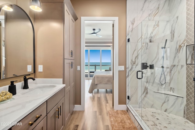 ensuite bathroom with wood finished floors, a water view, vanity, a marble finish shower, and ceiling fan