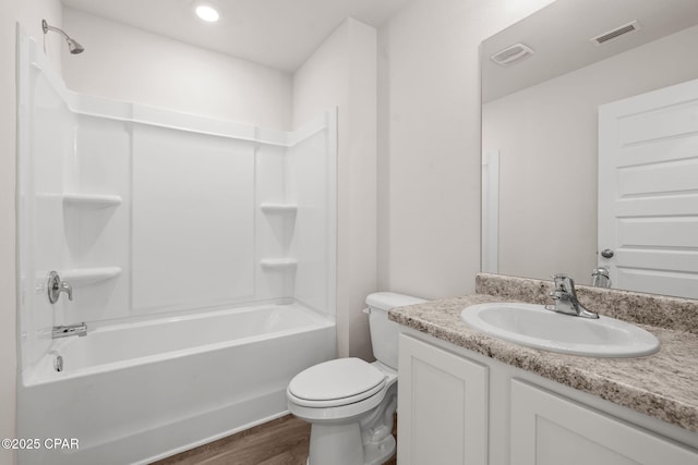 bathroom with vanity, toilet, wood finished floors,  shower combination, and visible vents