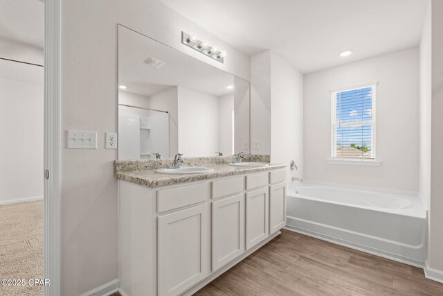 bathroom with double vanity, a sink, a garden tub, and wood finished floors