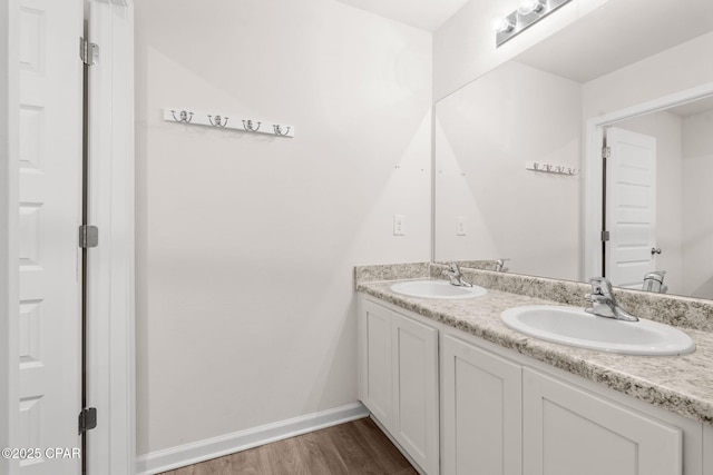 full bath with double vanity, a sink, baseboards, and wood finished floors