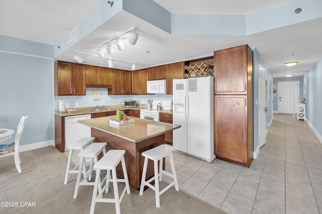 kitchen featuring a sink, white appliances, a breakfast bar area, visible vents, and a kitchen island