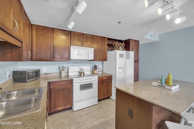 kitchen with a sink, white appliances, light stone counters, track lighting, and light tile patterned floors