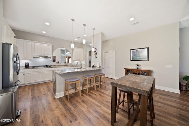 kitchen with a sink, a breakfast bar area, white cabinets, and arched walkways