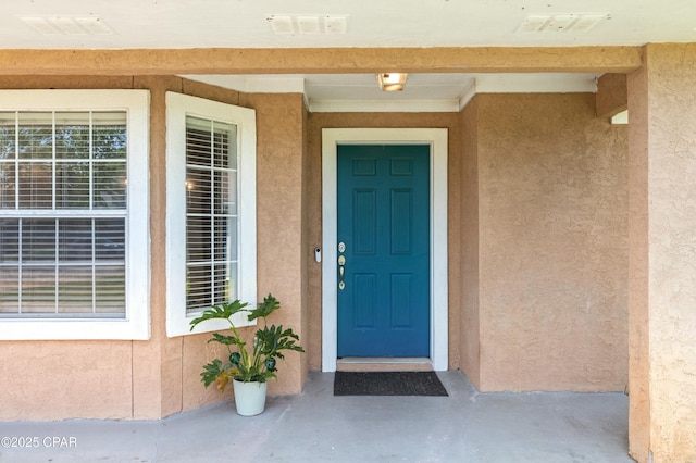 doorway to property with stucco siding and visible vents