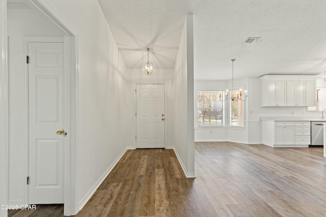 entrance foyer with a textured ceiling, light wood-type flooring, baseboards, an inviting chandelier, and visible vents